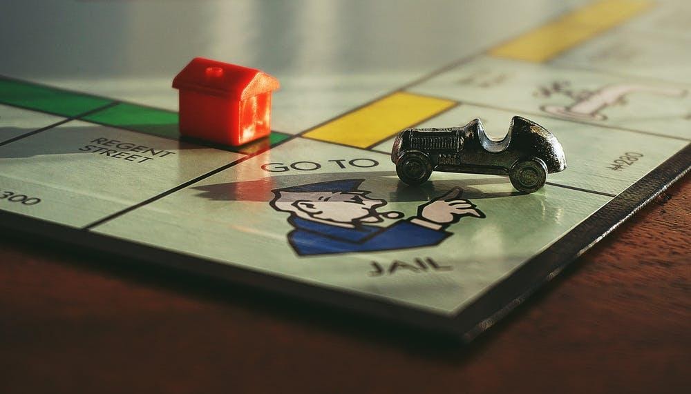 A monopoly board showing the car piece and the house piece at the "go to jail' section.