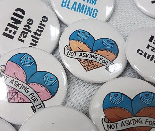 A collection of pin badges with slogans such as "consent is hot, rape is not"
