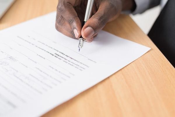 A hand with pen about to sign on paper. 