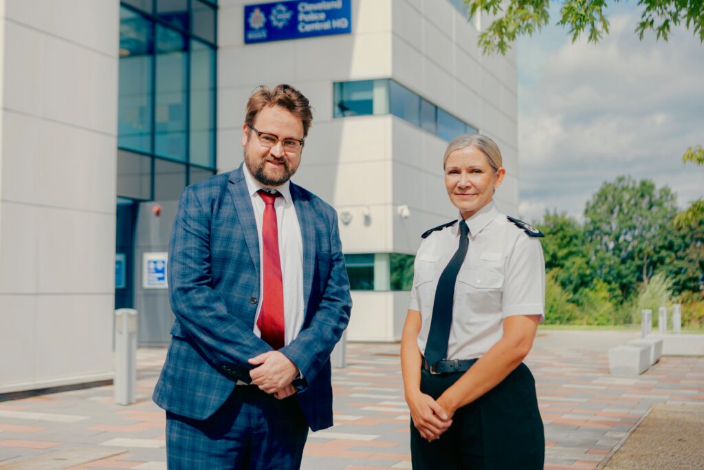 PCC Matt Storey and Chief Constable Victoria Fuller stood outside of Cleveland Police HQ. They both have their hands clasped in front of their bodies and are smiling. The Chief Constable is wearing police uniform.