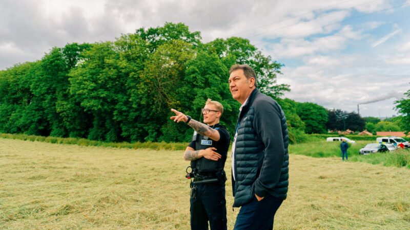PCC Steve Turner is standing in a field with a police officer. The officer is pointing into the distance.