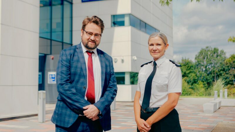 PCC Matt Storey and Chief Constable Victoria Fuller stood outside of Cleveland Police HQ. They both have their hands clasped in front of their bodies and are smiling. The Chief Constable is wearing police uniform.